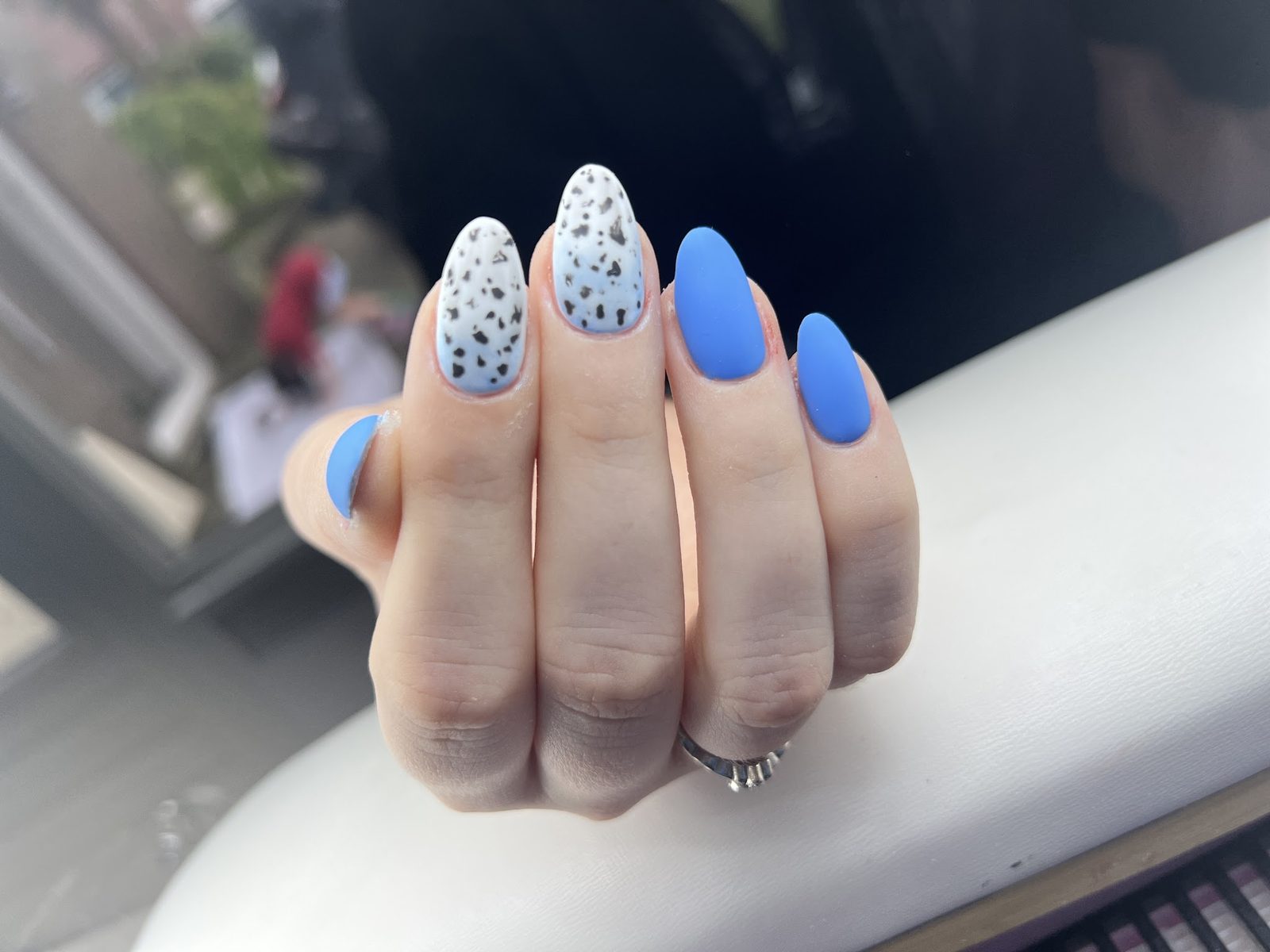 Amandelnagels in blauw, met twee witte nagels vol donkere stippen